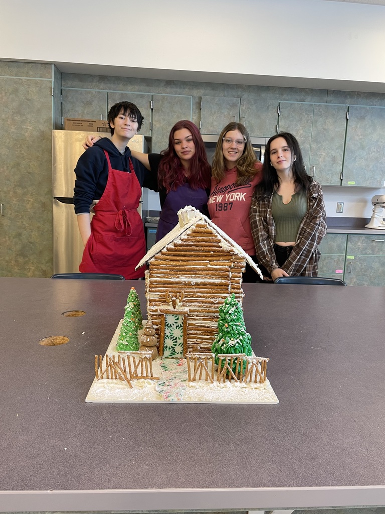 Four students stand behind a gingerbread house
