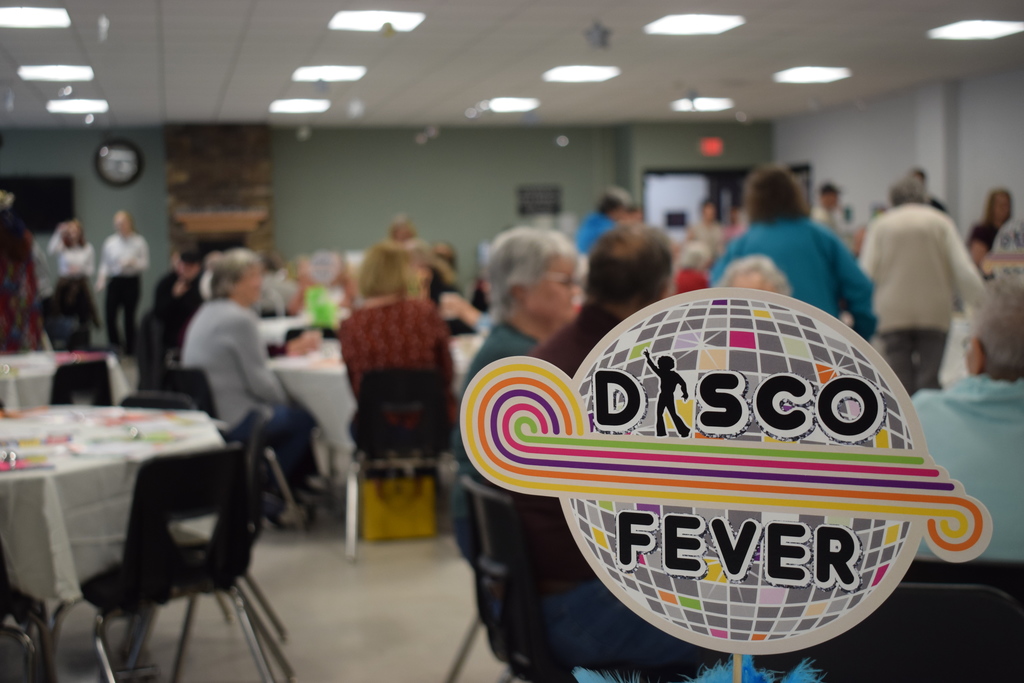 Seniors sit at tables with a disco fever sign